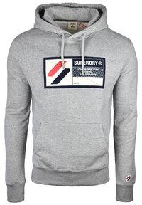 Sudadera con capucha gris hecha de una mezcla de algodón, que presenta un bolsillo tipo canguro en la parte delantera y un parche gráfico con logotipo en rojo, negro y blanco.