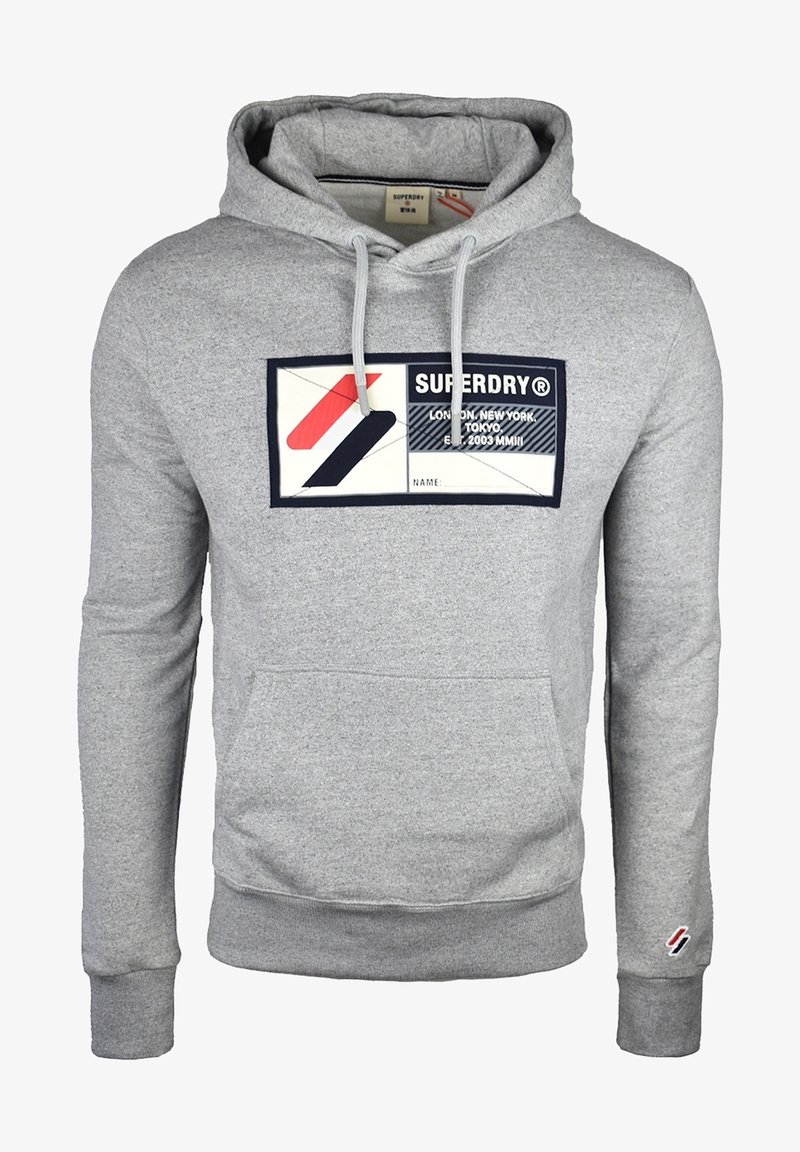 Sudadera con capucha gris hecha de una mezcla de algodón, que presenta un bolsillo tipo canguro en la parte delantera y un parche gráfico con logotipo en rojo, negro y blanco.