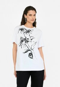 Tricou alb din bumbac cu un design floral negru. Mâneci scurte și decolteu rotund. Asortat cu pantaloni negri.