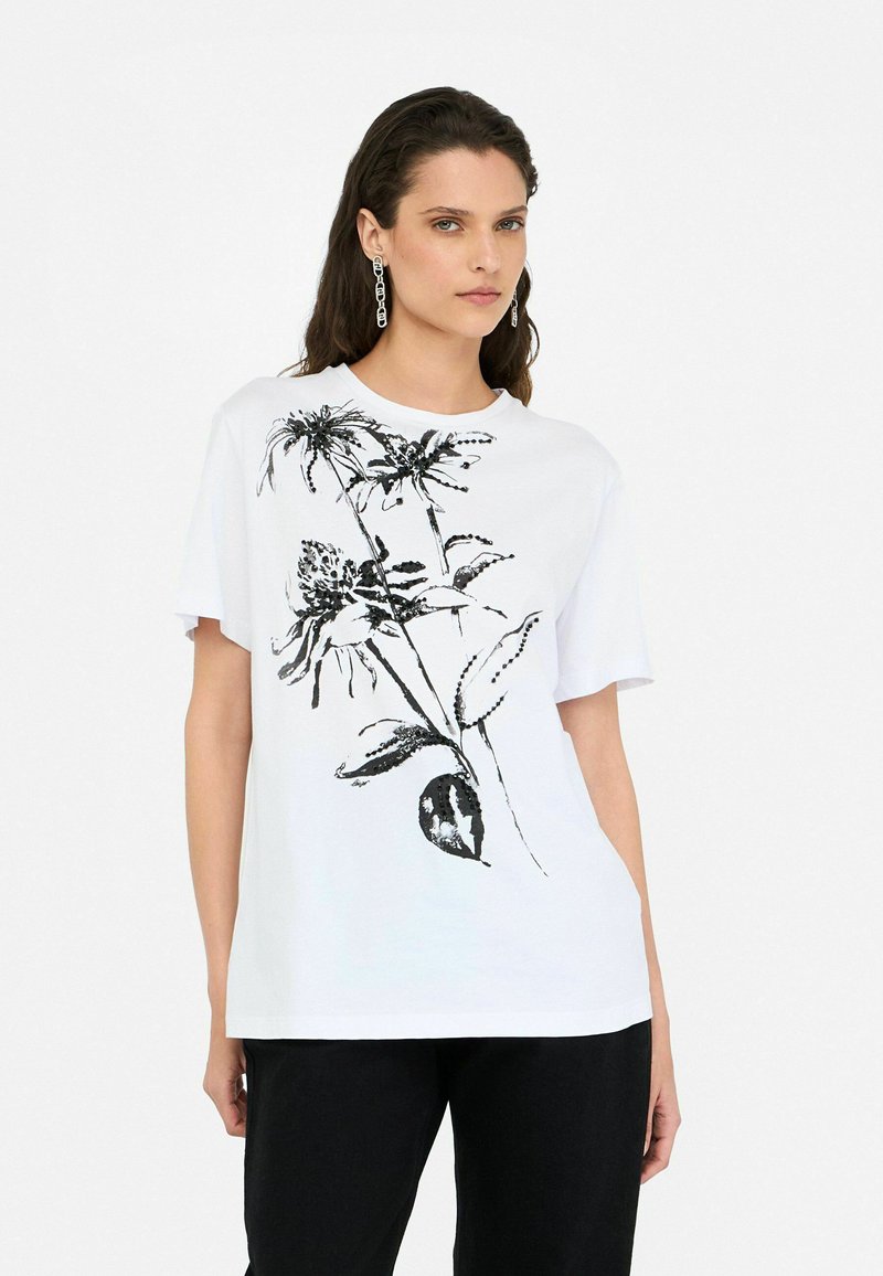 Tricou alb din bumbac cu un design floral negru. Mâneci scurte și decolteu rotund. Asortat cu pantaloni negri.