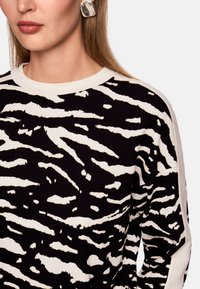 Black and white striped sweater with a ribbed crew neckline and long sleeves, featuring an abstract animal print pattern.