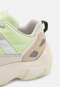 Sportliche Sneaker mit einem strukturierten, hellgrünen Mesh-Obermaterial, beige Velourleder-Akzenten, weißen Streifen und einer klobigen, off-white Sohle mit grünem Rand.