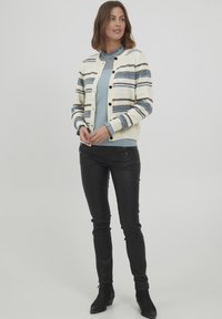 Adīta džemperis krēmkrāsā ar ziliem un brūniem svītrainiem, ar apaļu kakla izgriezumu un pogām. Saskaņots ar melnām ādas biksēm un potīšu zābakiem.