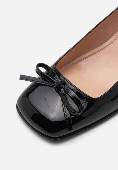 Schwarze Lackleder-Ballerinas mit abgerundeter Zehenpartie, die vorne mit einer kleinen Schleife verziert sind und ein glattes Innenfutter haben.