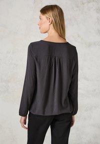 Blusa grigia scura con maniche lunghe, leggero brillantezza e motivo geometrico texture. Presenta una vestibilità comoda e un dettaglio arricciato sul retro.