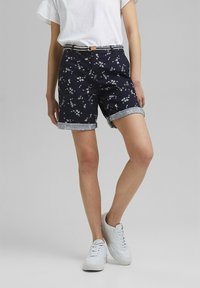 Námořnické šortky s bílým květinovým vzorem, s ohrnutými lemy a kontrastním pruhovaným opaskem. Vyrobeny z bavlny s hladkou texturou.