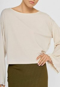 Lys beige ribbet crop top med brede ærmer og flæser ved manchetterne, parret med en mørk olivengrøn ribbet nederdel. Blød tekstur og afslappet pasform.