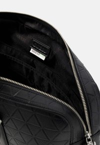 Zaino nero con motivo triangolare testurizzato, cerniera argentata e fodera in tessuto nero con etichetta "GUESS" e scomparti.