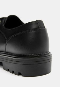 Sort lædersko med glat tekstur, rundet design og en tyk, ribbet gummisål med synlige slidmønstre.