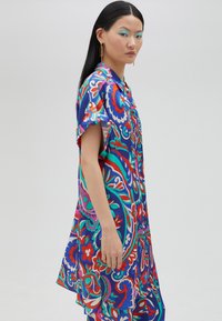 Vestido camisero de manga corta y colorido que presenta un vibrante estampado floral y de paisley en azul, rojo y rosa sobre una tela ligera.