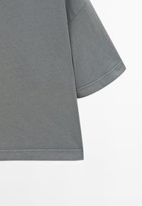 Grå kortærmet t-shirt i blødt bomuldsstof, med en rund kant og subtile syningsdetaljer. Glat tekstur med en afslappet pasform.