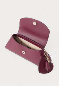 Paarse gestructureerde clutch met open klep, gouden hardware en een sleutelhanger met een hartvormige accent. Interieur bevat een ritsvak.