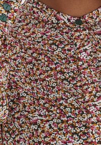 Tessuto con motivi floreali in tonalità di rosa, marrone e bianco, con piccoli bottoni verdi e una consistenza morbida arricchita da dettagli plissettati.