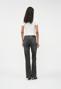 Jean noir évasé à taille haute, avec une texture lisse, un design classique à cinq poches, associé à un haut blanc ajusté.