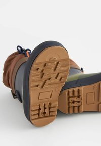 Bottes d'hiver imperméables avec un dessus marron et des accents bleu marine. La semelle en caoutchouc présente un motif de grip texturé. Lacets ajustables pour un maintien sécurisé.
