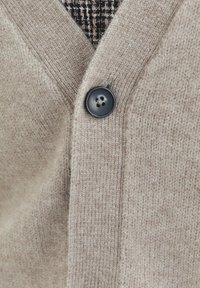 Cardigan in maglia beige con scollo a V, tessuto testurizzato e un bottone nero rotondo nella parte frontale. Dettagli di cucitura sottili visibili.