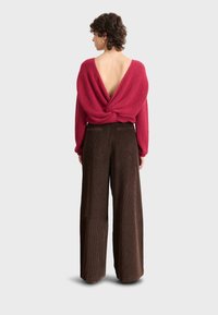 Bordo textured pleteni pulover s niskim leđima i prevrnutim dizajnom, uparen s širokim smeškim baršunastim hlačama.