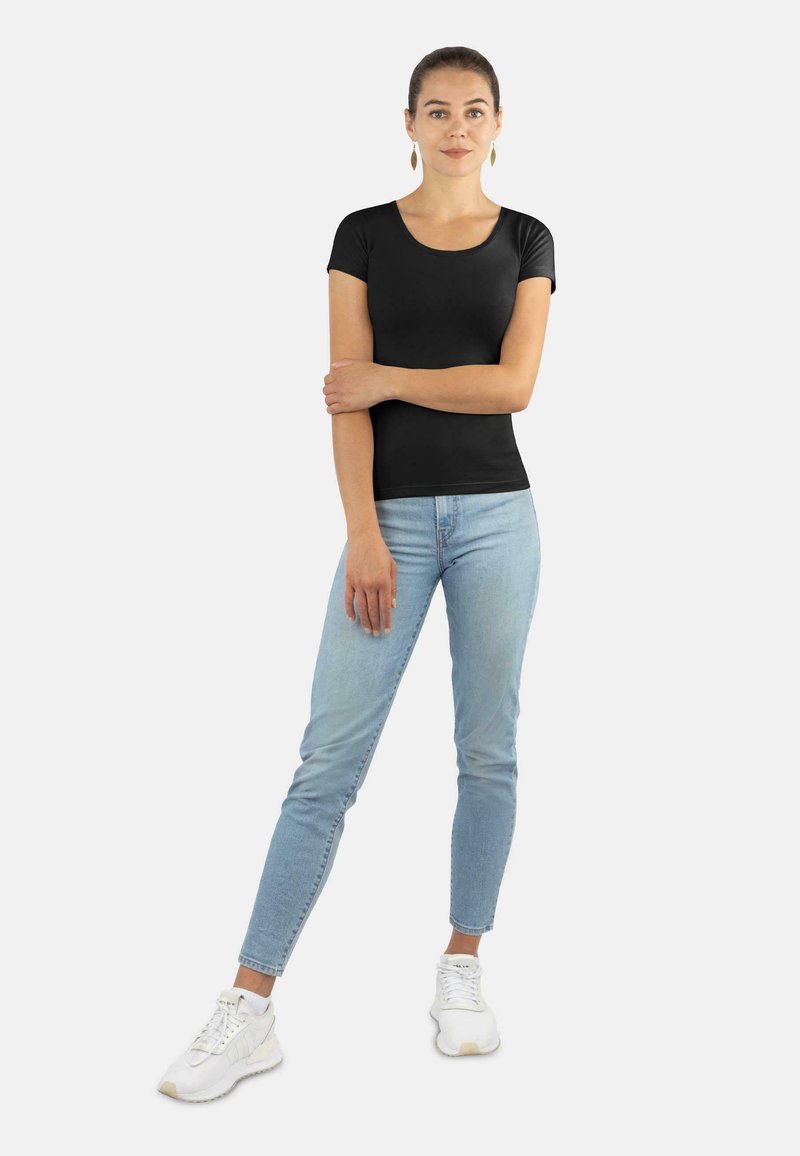 Schwarzes, kurzärmliges, eng anliegendes T-Shirt, kombiniert mit hellblauen Skinny-Jeans und weißen Sneakern. Minimalistisches Design mit glatter Stoffstruktur.