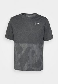 Camiseta de color gris oscuro con el logo blanco de Nike, mezcla de tela sólida y estampada con detalles a rayas en la parte inferior, diseño de cuello redondo.