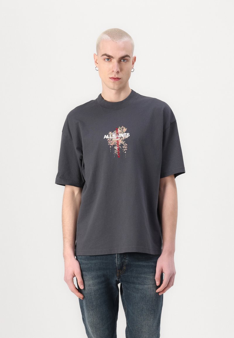 Camiseta gris de manga corta con un gráfico floral y texto en el centro. Hecha de algodón, tiene un corte relajado y un cuello redondo.