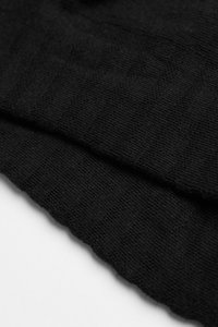 Schwarzer Strickstoff mit einer strukturierten Oberfläche und einem wellenförmigen Rand. Das Material wirkt weich und leicht, ideal für Lagenlooks oder Freizeitbekleidung.