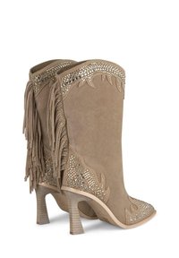 Las botas de ante de estilo western en tono marrón presentan detalles de flecos, adornos metálicos y tacones esculpidos con un acabado texturizado.