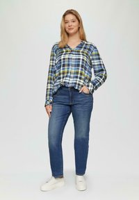 Geruit overhemd in blauw, geel en wit, gedragen met blauwe spijkerbroek en witte sneakers, met lange mouwen en een comfortabele pasvorm.
