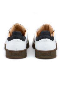 Weiße Ledersneaker mit brauner Gummisohle, schwarzer Fersenschlaufe und cremefarbenem Innenraum. Verfügt über ein Logo an der Ferse und strukturierte Details.