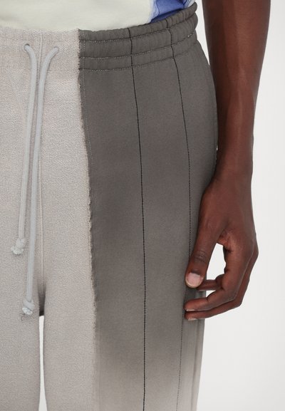 Gray and beige two-tone sweatpants with a textured finish, featuring an elastic waistband, drawstring, and contrasting stitching details.