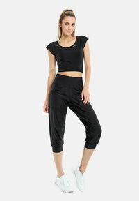 Sort cropped top med korte ærmer, parret med sorte cropped bukser med en elastisk talje og opsmøgede ben. Hvide sportssko.