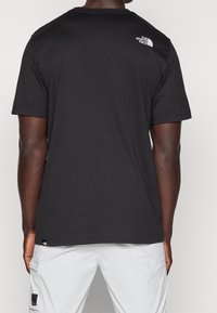 Czarny bawełniany T-shirt z krótkimi rękawami, okrągłym dekoltem oraz białym logo na górnej części pleców. Prosty dół oraz luźny krój.