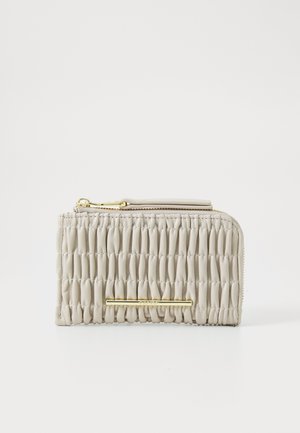 Porte-monnaie zippé beige avec texture matelassée, accents en métal doré et finition lisse. Il présente un design fin et une fermeture à glissière pratique.