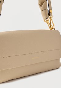 Šviesiai rudos odos peties rankinė su lygiu paviršiumi, auksinėmis detalėmis ir įspaustu logotipu. Turi paminkštintą dirželį patogumui.