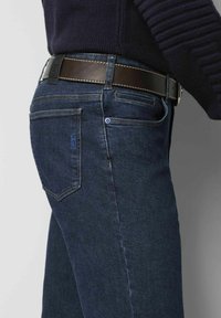 Donkerblauwe denim jeans met een recht model, gedetailleerde stiksels, vier zakken en een bruine leren riem met een zwarte gesp.