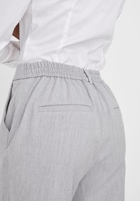 Grå elastiske bukser med teksturert overflate, med sidelommer og en baklomme, stylet med en hvit skjorte.