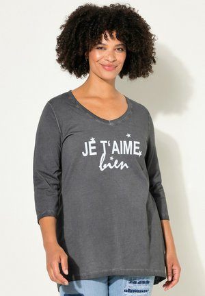 Grijze langemouw T-shirt met een V-hals en witte bedrukte tekst "JE T'AIME bien," met sterren. Zacht materiaal, ontspannen pasvorm en zichtbare stiksels.