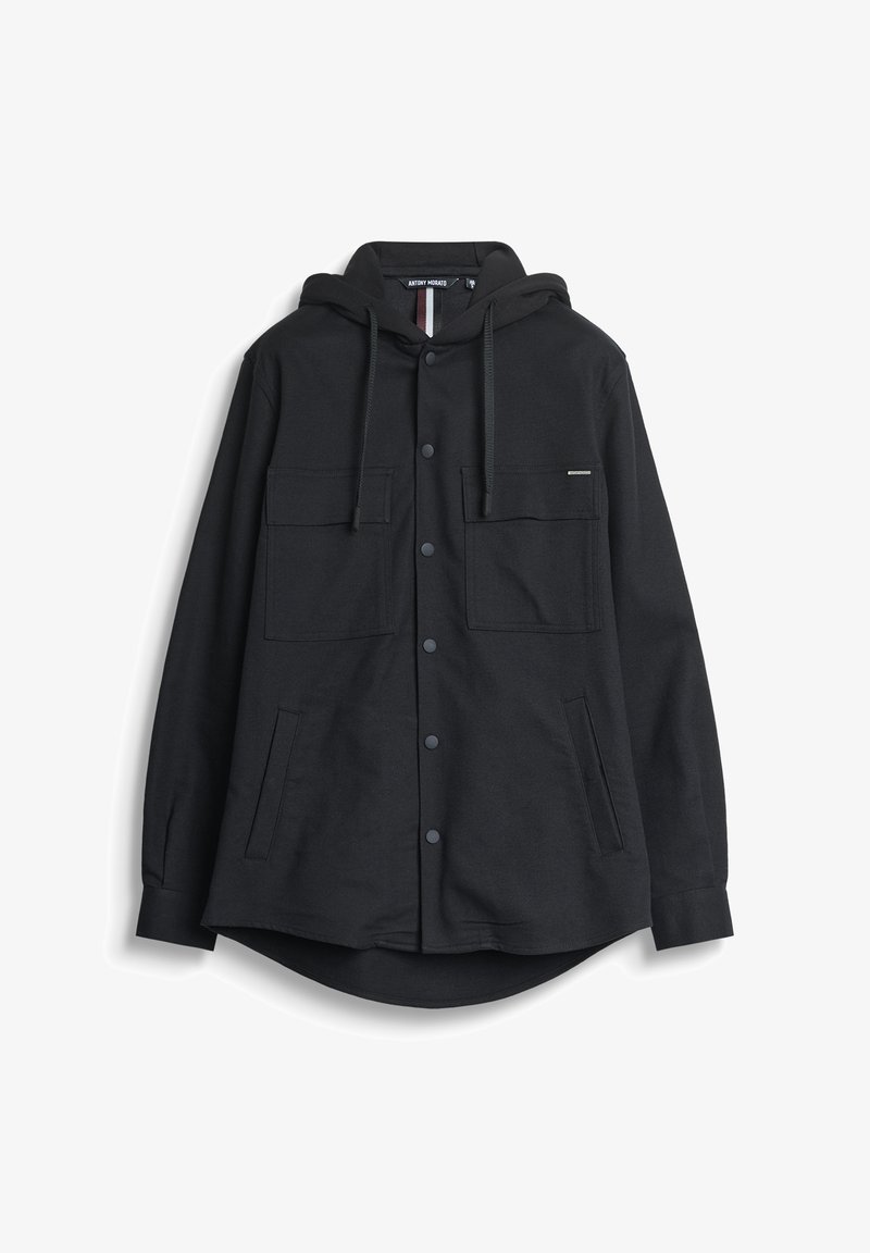 Crna majica sa kapuljačom od mekog materijala, koja ima dvije džepove na prsima, bočne džepove i blago zakrivljen donji rub. Suptilan logo detalj na izrezu.