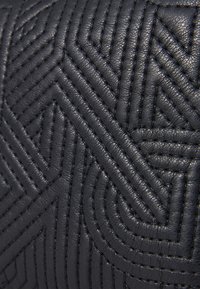 Pelle nera con un motivo geometrico testurizzato. Il design presenta cuciture rialzate a zigzag, creando profondità e dettaglio.