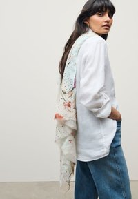 Kerge, mustriline sall pastelsed toonides, lillemotiivide ja peente täpiornamentidega; langeb valgele, lõtvalt istuvale särkile.