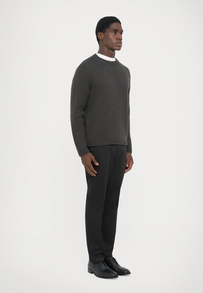 Dark gray knit sweater with a round neckline, paired with black trousers and black shoes, featuring ribbed cuffs and hem.