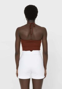 Bruine geribde haltertop met verstelbare strik bij de hals, gecombineerd met aansluitende witte shorts met hoge taille en uitsnijding aan de achterkant.