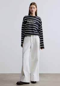 Navyblauw met witte gestreepte longsleeve met de tekst "Barbour EST. 1894", gecombineerd met witte, hoogwater, wijde broekspijpen en zwarte schoenen.