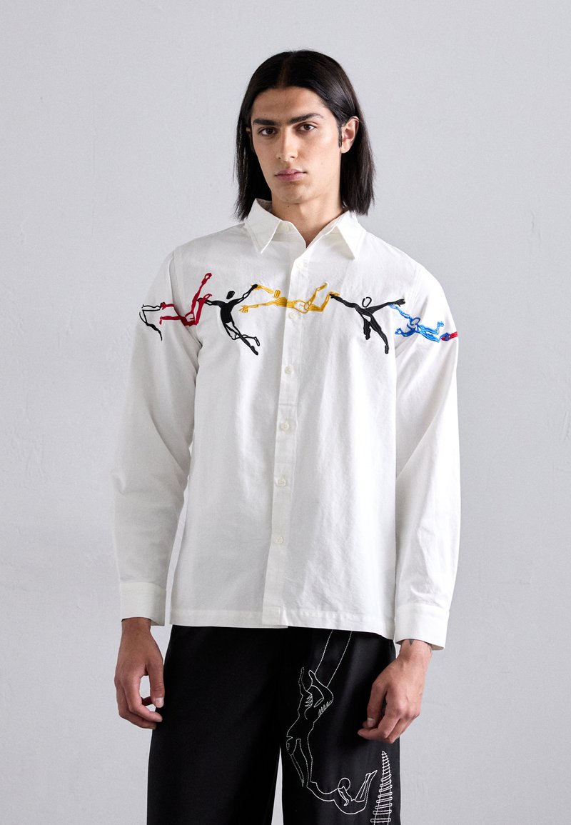 White long-sleeve shirt with button closure, featuring colorful embroidered figures in red, yellow, blue, and black along the shoulders.