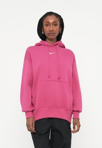 Rožna kapuca s prednjim žepom in vrvico. Ima bel Nike logotip na prsih. Narejena je iz mehkega, teksturiranega materiala.