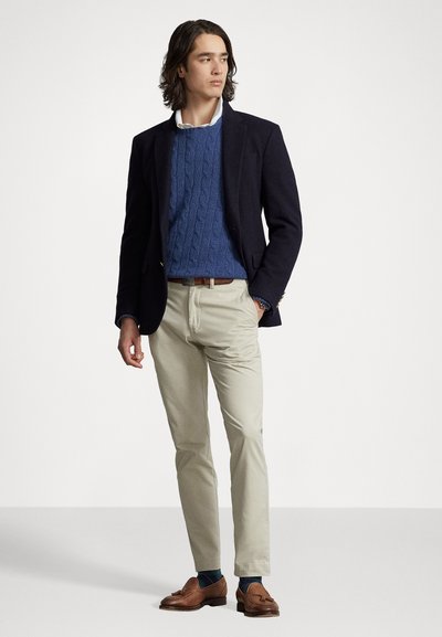 Marineblazer over en blå kabelstrikket genser, beige chinos, brune loafers og blå sokker, med en glatt tekstur og skreddersydd passform.