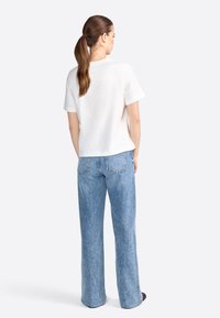 Top blanco de manga corta y jeans de pierna ancha azul claro. El top tiene un corte holgado y un escote redondo, mientras que los jeans cuentan con bolsillos traseros y una textura desgastada.