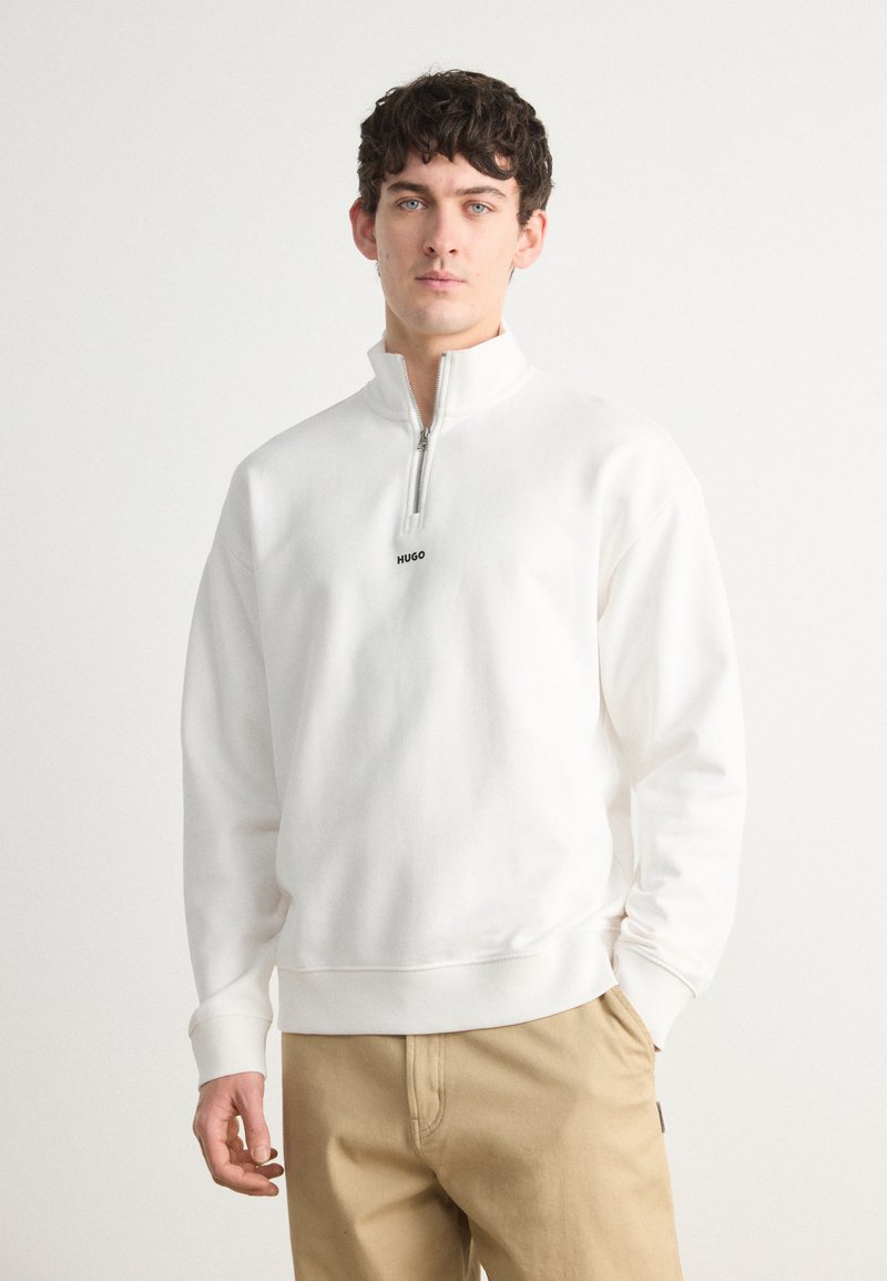 Hvit zip-neck sweatshirt med subtil elastisk linning og mansjetter, med en liten svart "HUGO"-logo på brystet. Standard passform.