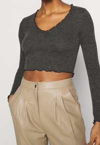 Szary, prążkowany, długi top z długim rękawem, z falistym dekoltem i dołem, w zestawieniu z beżowymi, wysokim stanem spodniami z imitacji skóry z zakładkami.