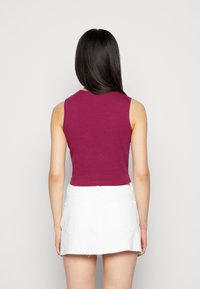 Top cropped sem mangas na cor bordô com decote redondo, em material de algodão. Combinado com uma saia de ganga branca com bolsos traseiros e bainha desfiada.