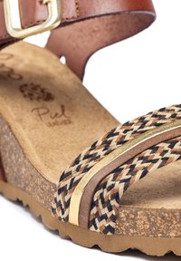 Sandalia de cuero marrón con una correa de textil trenzada en beige, marrón y negro con detalles dorados. Suela de corcho con acabado texturizado.